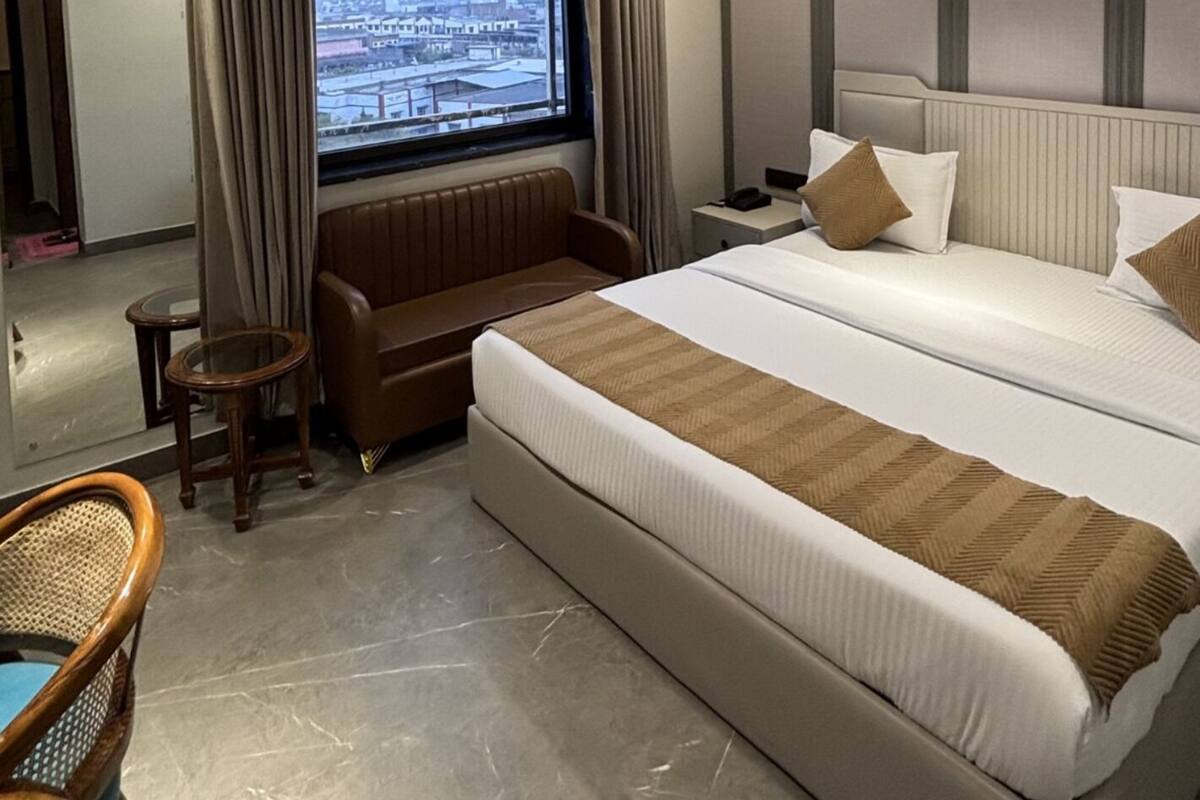 A hotel room with a bed, a seating area, a window with a city view, and a ceiling fan.