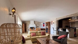 Un vaste espace de vie comprenant un canapé, une table basse en bois, une lampe en osier et une cheminée en pierre.