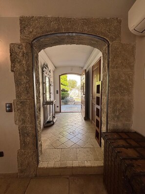 Ein steiner Torbogen führt in einen gefliesten Gang mit Blick auf Grünflächen.