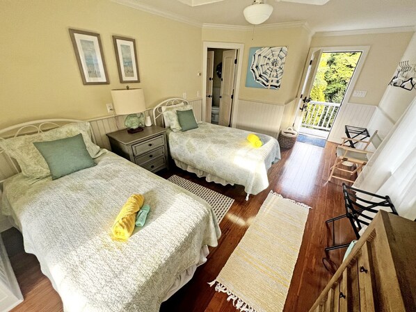 A bedroom with two beds, a wooden floor, a door leading outside, and a view of greenery.