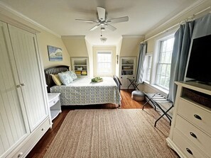 Un dormitorio con una cama, ventilador de techo, ventana con cortinas, cómoda y televisor.