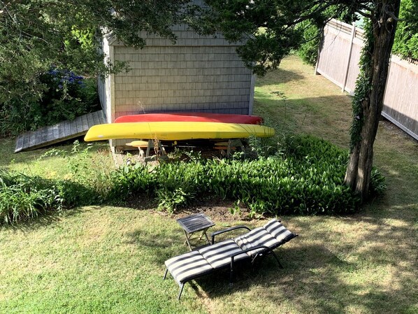 A backyard with a patio table, a striped lounge chair, and a yellow umbrella.