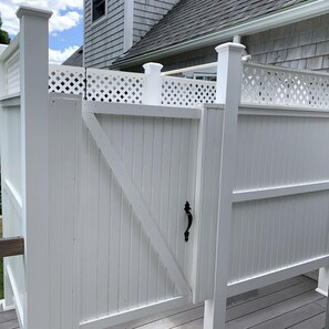 A white wooden deck with a white picket fence, a metal gate, and a house in the background.