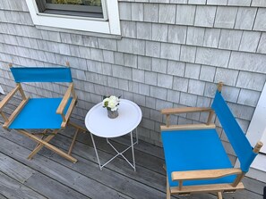 A deck with two blue cushioned chairs and a small white table with a vase of flowers.