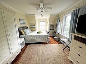 A bedroom with a bed, a ceiling fan, a window with curtains, a dresser, and a television.