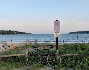 A beach with a bicycle, a sign indicating resident recreation permit or daily pass requirement, and a sign advising to keep off dunes.