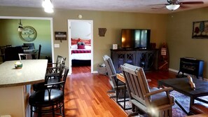A living room with a TV, dining area with chairs, a kitchen area with a table and chairs, and a door labeled 'River House'. - Deck of Dreams: Cabin with Unrivaled River Views in Arkansas (Calico Rock)