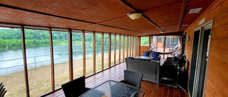 Een houten terras met een glazen tafel en stoelen, met uitzicht op een rivier.