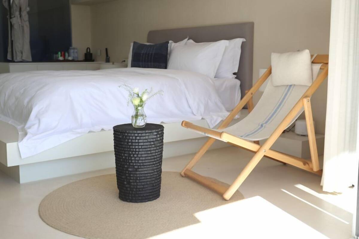 Ein Schlafzimmer mit einem Bett, einem kleinen Tisch mit einer Vase, einem Sessel und einem runden Teppich.