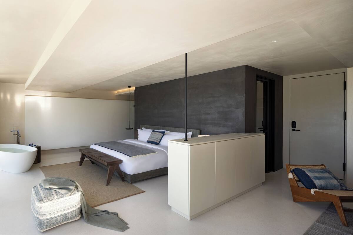 Ein modernes Schlafzimmer mit einem großen Bett, einem Nachttisch, einer Bank, einer Couch, einer Badewanne und einem Kleiderschrank.