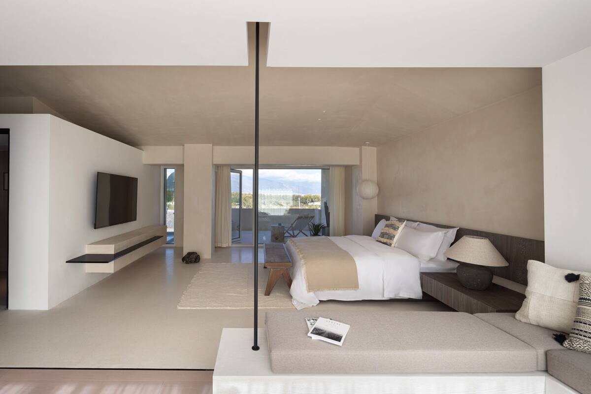 Ein modernes Hotelzimmer mit Bett, Sofa, Fernseher und einem Balkon mit Blick.