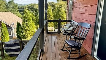 A wooden deck with two rocking chairs and a view of a forested area.