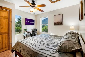 Ein Schlafzimmer mit Bett, Schreibtisch, Stuhl, Deckenventilator, Fernseher und einem Fenster mit Blick.