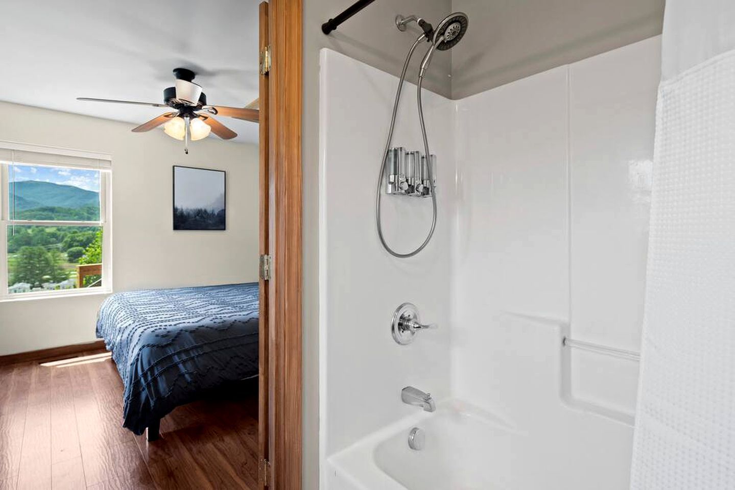 A bedroom with a bed, a ceiling fan, a window with a view, and a bathroom with a shower.
