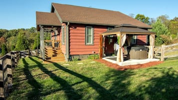 A red wooden house with a covered porch, a hot tub, and a wooden fence.