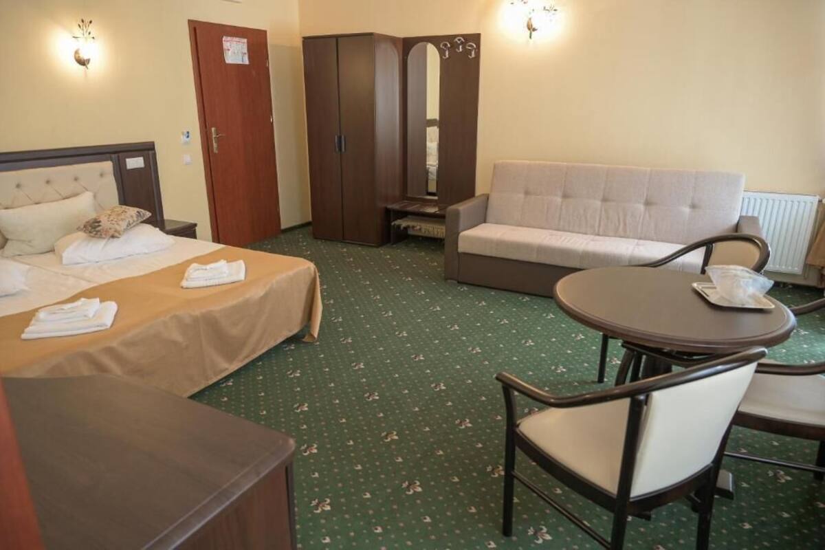 A hotel room with a bed, a sofa, a dining table, and a wardrobe.