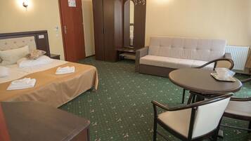A hotel room with a bed, a sofa, a dining table, and a wardrobe.