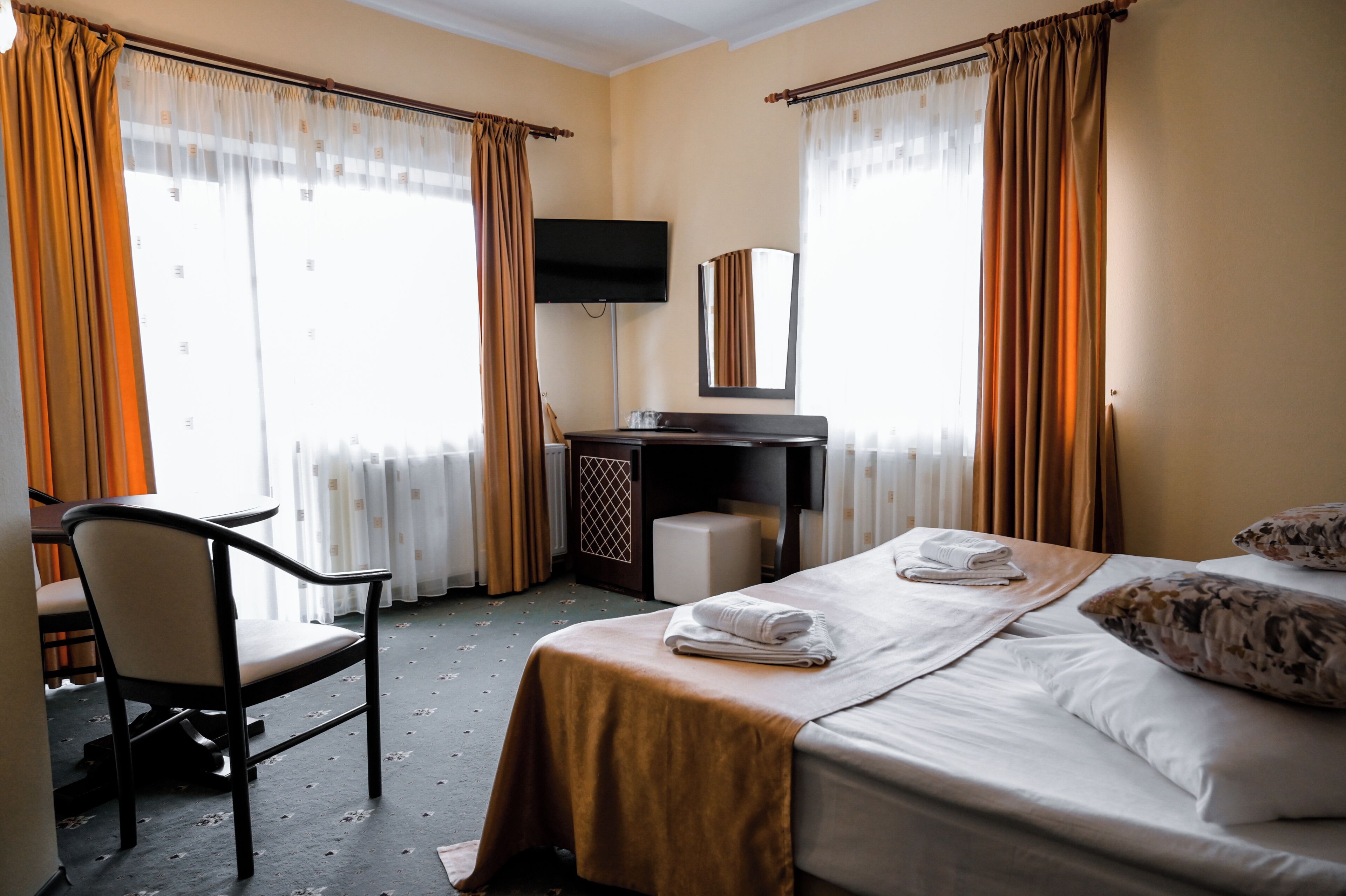 Habitación de hotel con cama, escritorio, silla, televisión y ventana con cortinas.