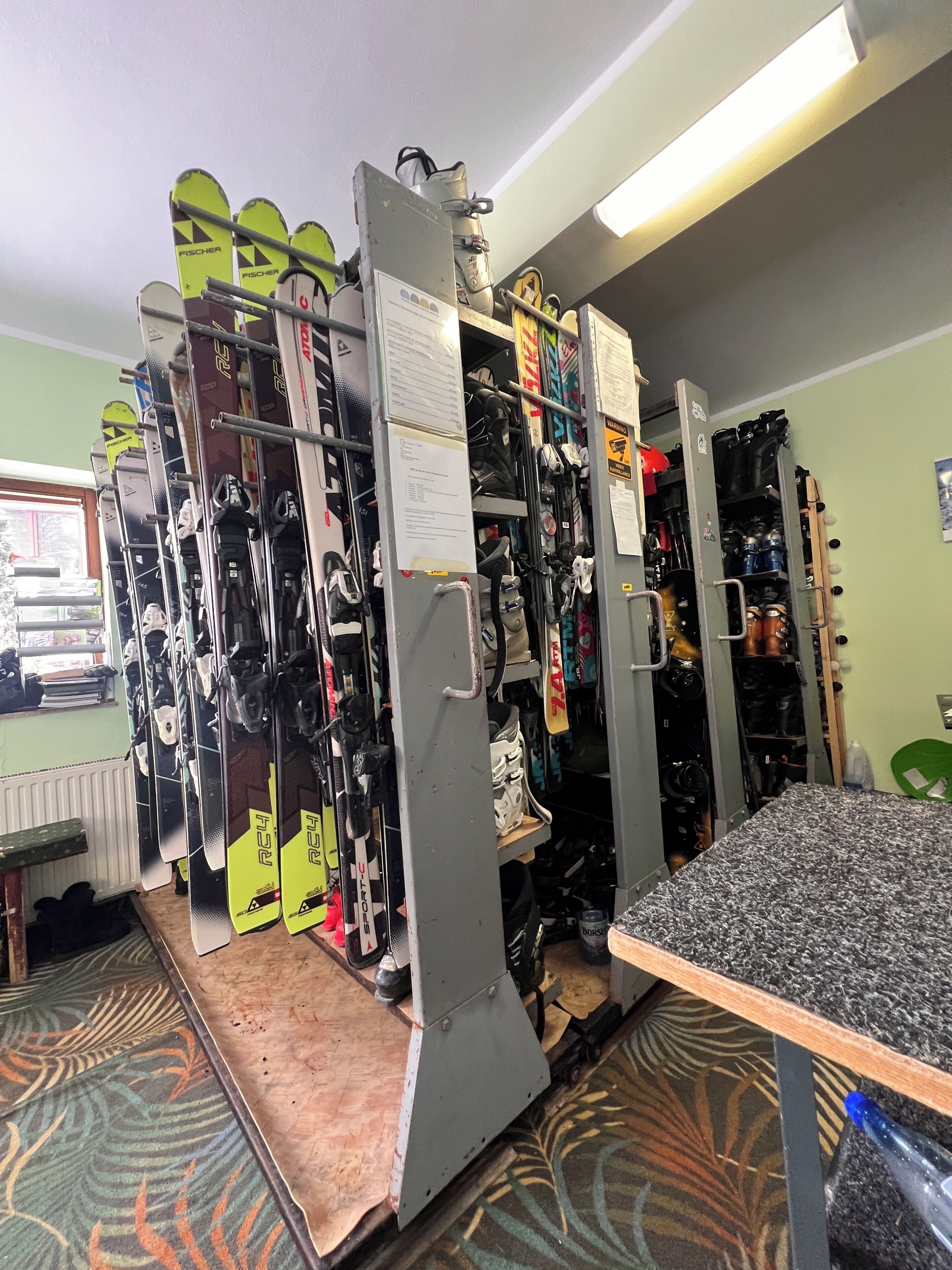 A ski equipment storage room with racks of skis and snowboards, a table, and a radiator.