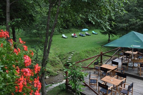 A deck with outdoor seating, a grassy area with lounge chairs, and a green umbrella.