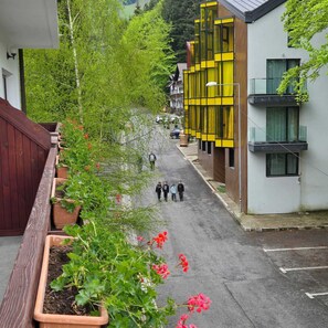 A narrow street with modern buildings, a wooden fence, and potted plants.