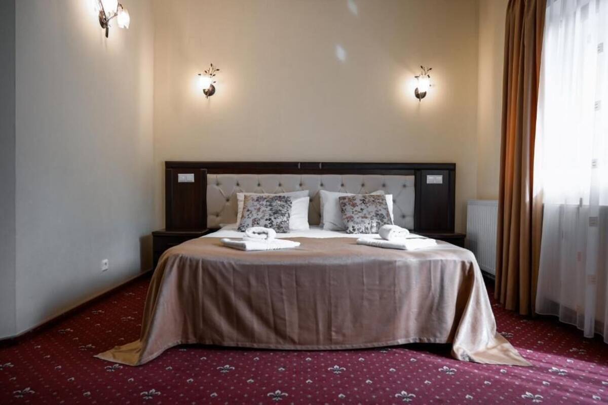 A hotel room with a large bed, two bedside tables, a headboard with light fixtures, and a window with curtains.