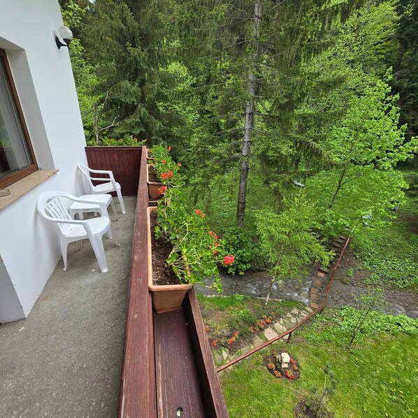 A balcony with a wooden planter, white plastic chairs, and a view of a forested area. - ANOTIMPURI (Predeal)
