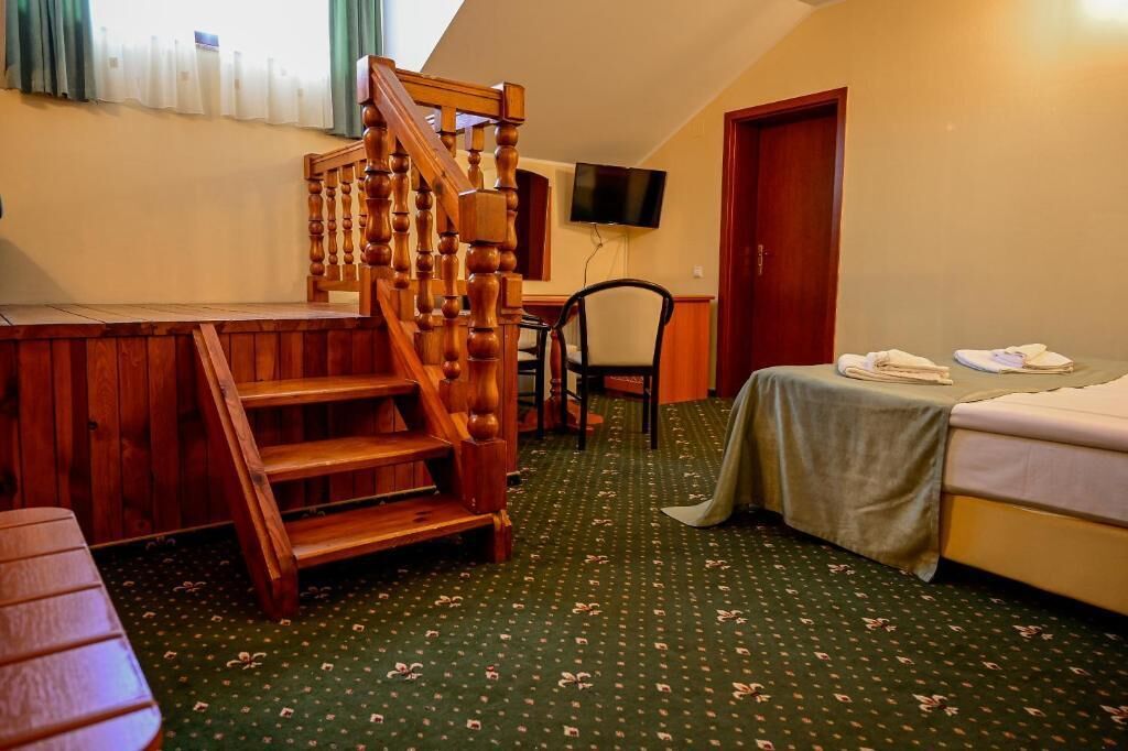A room with a wooden staircase, a bed, a table, a chair, and a television on the wall.