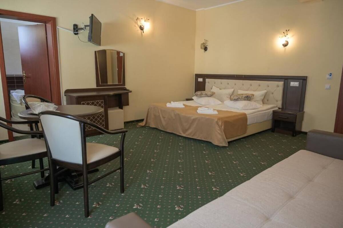 A hotel room with a bed, a desk with a chair, a television, and wall-mounted lights.