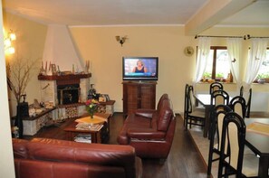 A living room with a fireplace, television, leather sofa, dining table, and chairs. - ANOTIMPURI (Predeal)