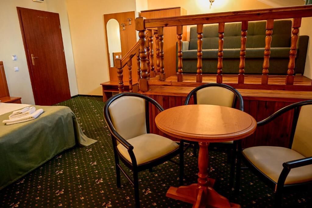 Une chambre d’hôtel avec un lit, une table ronde en bois, deux chaises, un escalier et un canapé vert.