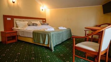 A hotel room with a bed, a chair, a nightstand, and a wall-mounted TV.