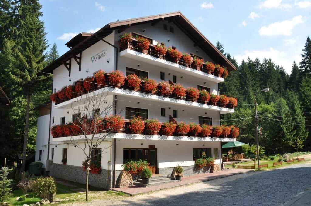 A multi-story hotel with balconies adorned with red flowers, a stone facade, and a cobblestone street.