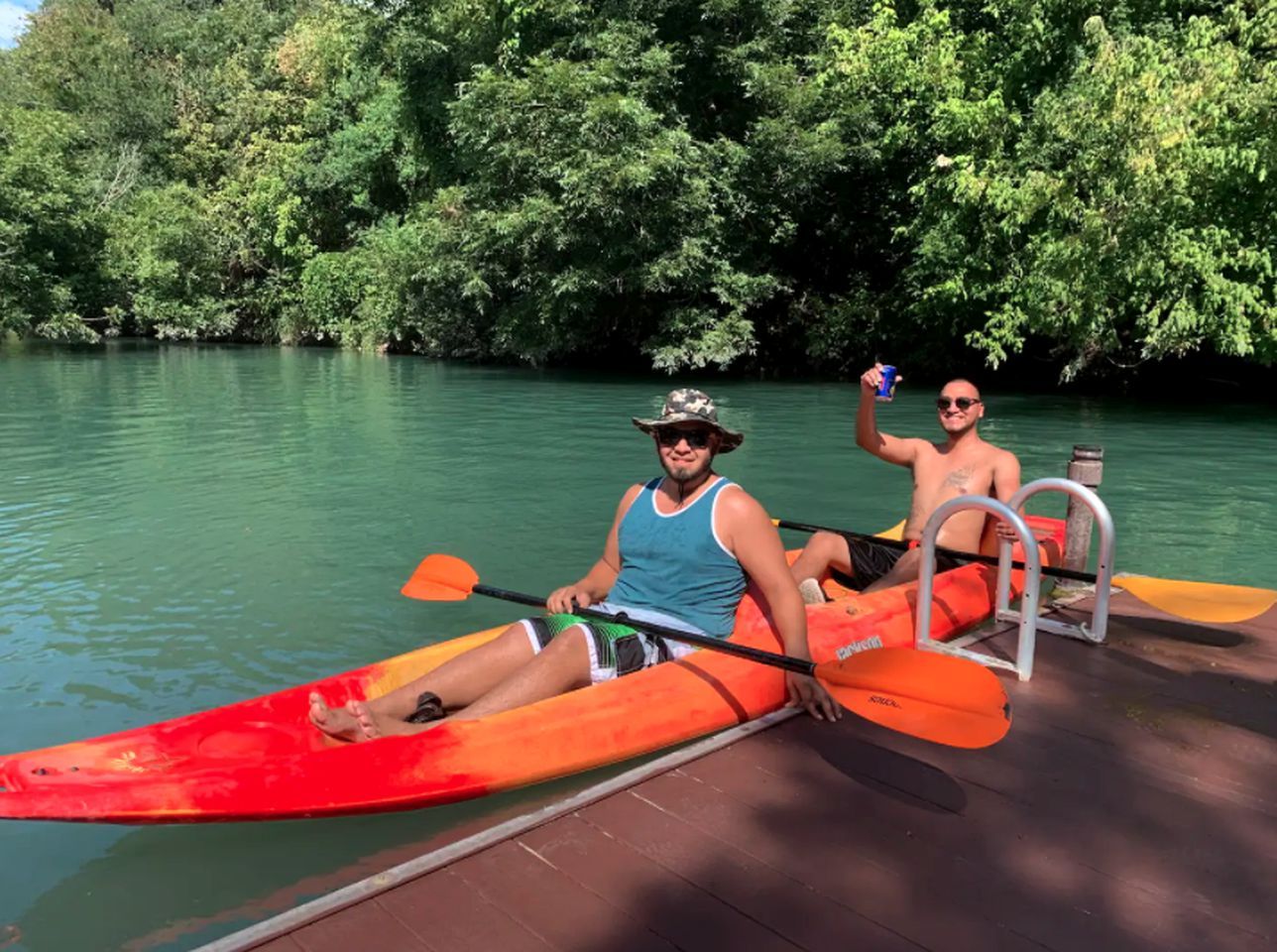 Two people in a canoe on a dock with a forested river in the background.