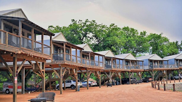 A series of wooden cabins with balconies, connected by a covered walkway, set in a natural environment with trees in the background. - Aquatic Retreat: Waterfront Tented Cabin with Full Amenities for Water Lovers in Cibolo, TX (Cibolo)