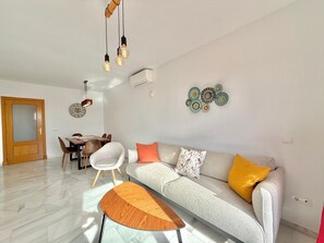A modern living room with a sofa, coffee table, and dining area. - Terrasol LAS Carmelitas 2 Dormitorios (Velez-Malaga)