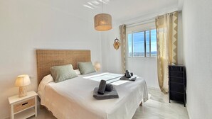 A bedroom with a bed, bedside tables, a lamp, a window with curtains, and a view. - Terrasol LAS Carmelitas 2 Dormitorios (Velez-Malaga)
