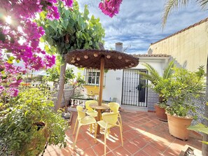 A patio with a round table and chairs, surrounded by potted plants and a thatched umbrella. - Terrasol LOS Nardos 229 (Velez-Malaga)