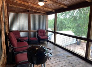 A covered porch with wicker chairs, a grill, and a view of the outdoors.