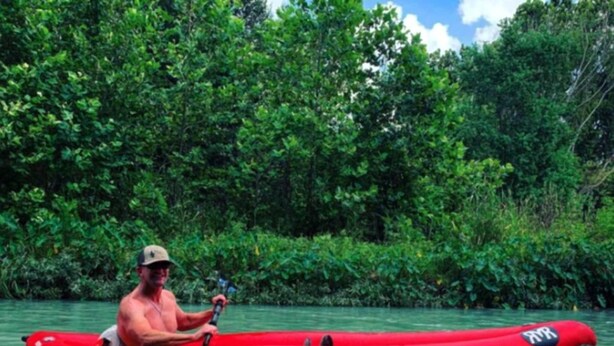 A person in a red kayak on calm water surrounded by dense greenery. - Perfect Glamping Getaway: A Stay in a Rustic Cabin by the San Marcos River near Kingsbury, Texas (Kingsbury)