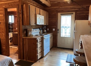 Ein Holzblockhaus Innenansicht mit Küchenbereich, inklusive Herd, Kühlschrank und Holzschränken.