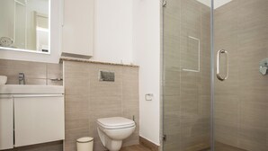 A bathroom with a toilet, a sink, a mirror, and a shower with a glass door. - ORAK - Minimalist Aparthotel with Gym & Pool in Lavington (Nairobi)