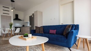 A modern living room with a blue sofa, a white coffee table, and a kitchen in the background. - ORAK - Minimalist Aparthotel with Gym & Pool in Lavington (Nairobi)