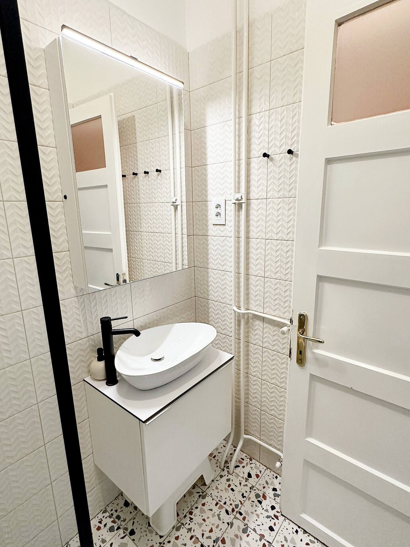 A bathroom with a white sink, a mirror, a shower, and a door.