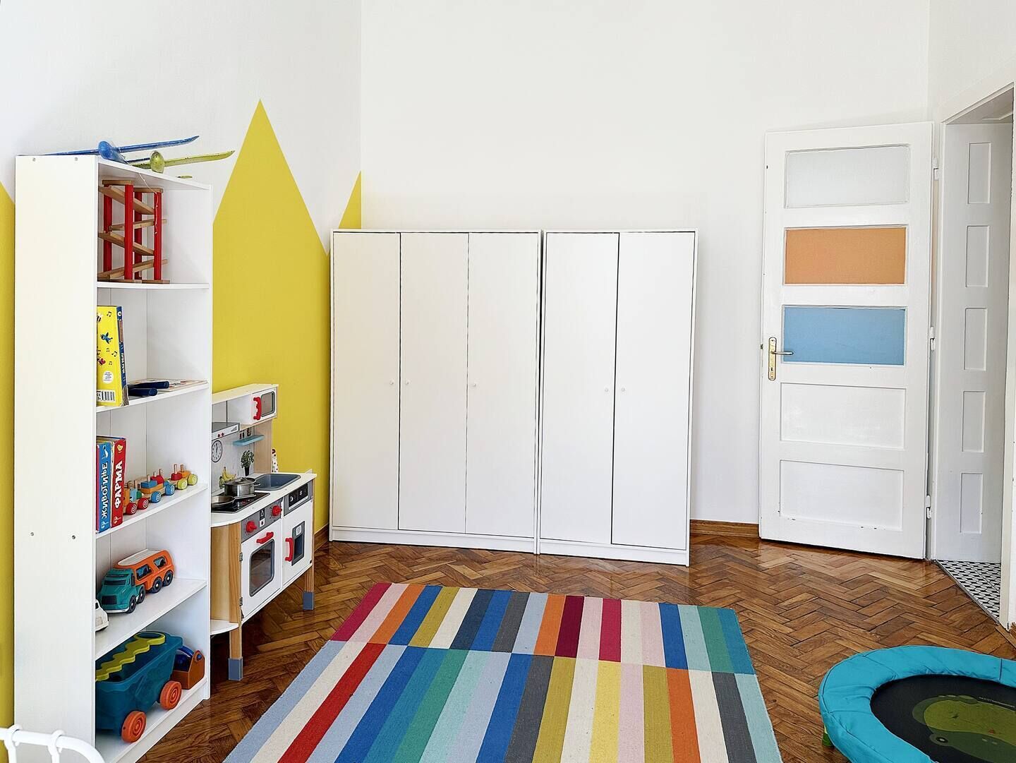 A room with a white wardrobe, a striped rug, and a toy kitchen set.