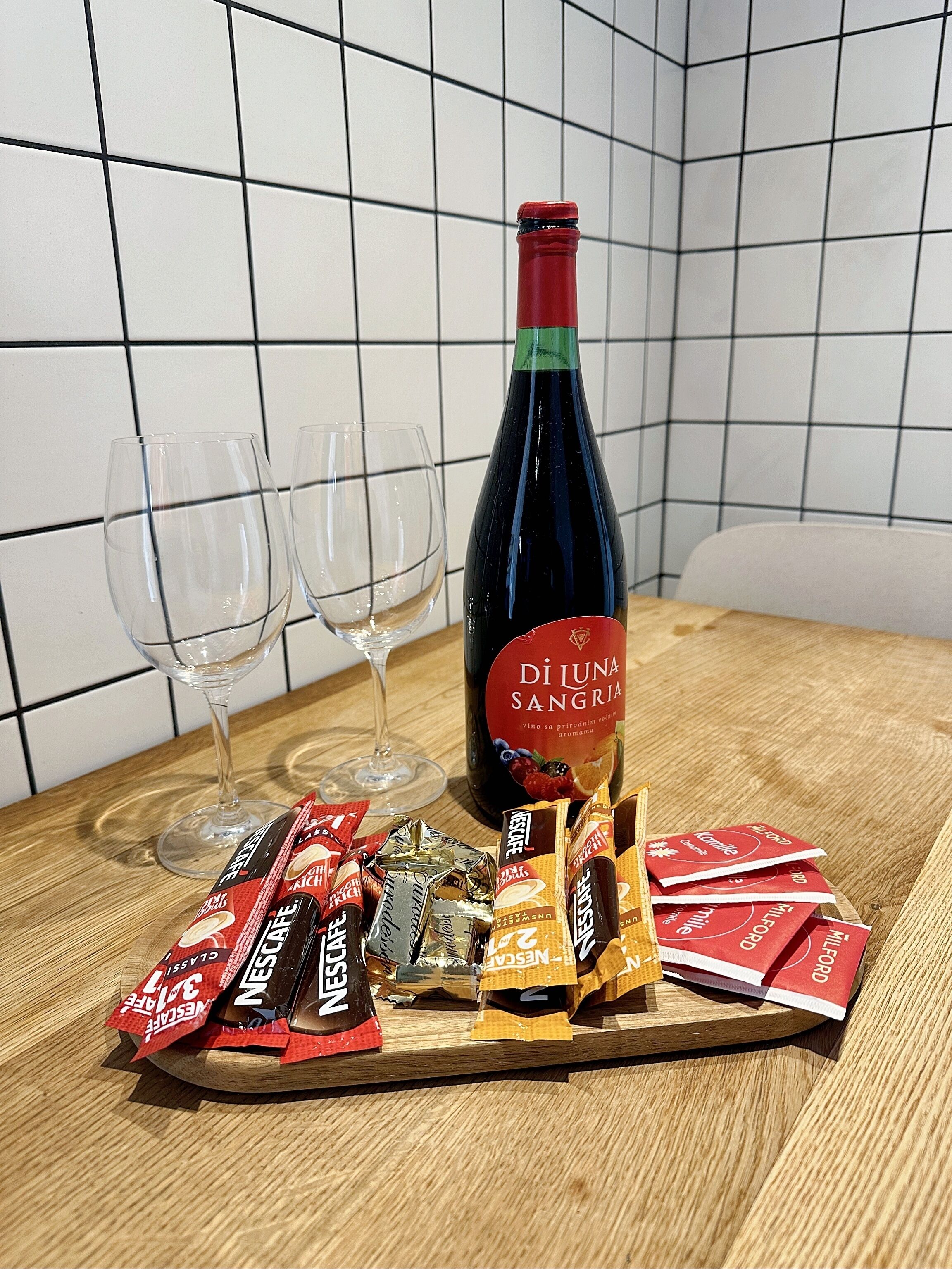 A bottle of wine, two glasses, and assorted chocolate bars on a wooden board.