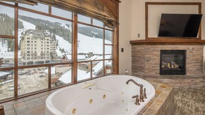 A large bathtub with a view of a ski resort through large windows. - New! Village Center Ski-In/Ski-Out 3-bed Suite! (Big Sky)