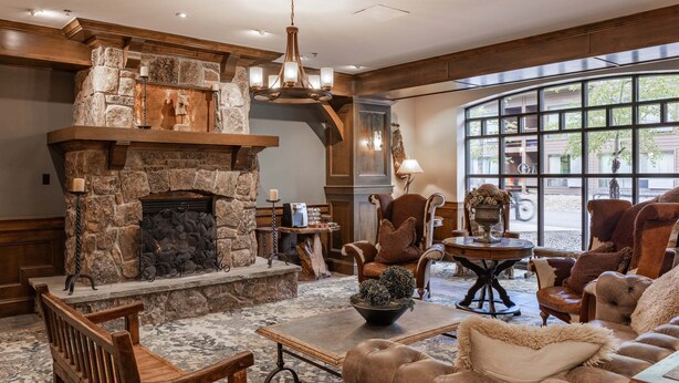 A cozy lounge area with a stone fireplace, leather furniture, and a large window offering a view of the outdoors. - New! Village Center Ski-In/Ski-Out 3-bed Suite! (Big Sky)