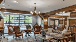 A spacious living area with a large window, wooden furniture, and a chandelier. - New! Village Center Ski-In/Ski-Out 3-bed Suite! (Big Sky)