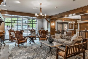A spacious living area with a large window, wooden furniture, and a chandelier.
